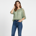 Model wearing CAbi pebble blue-green print blouse on white studio background